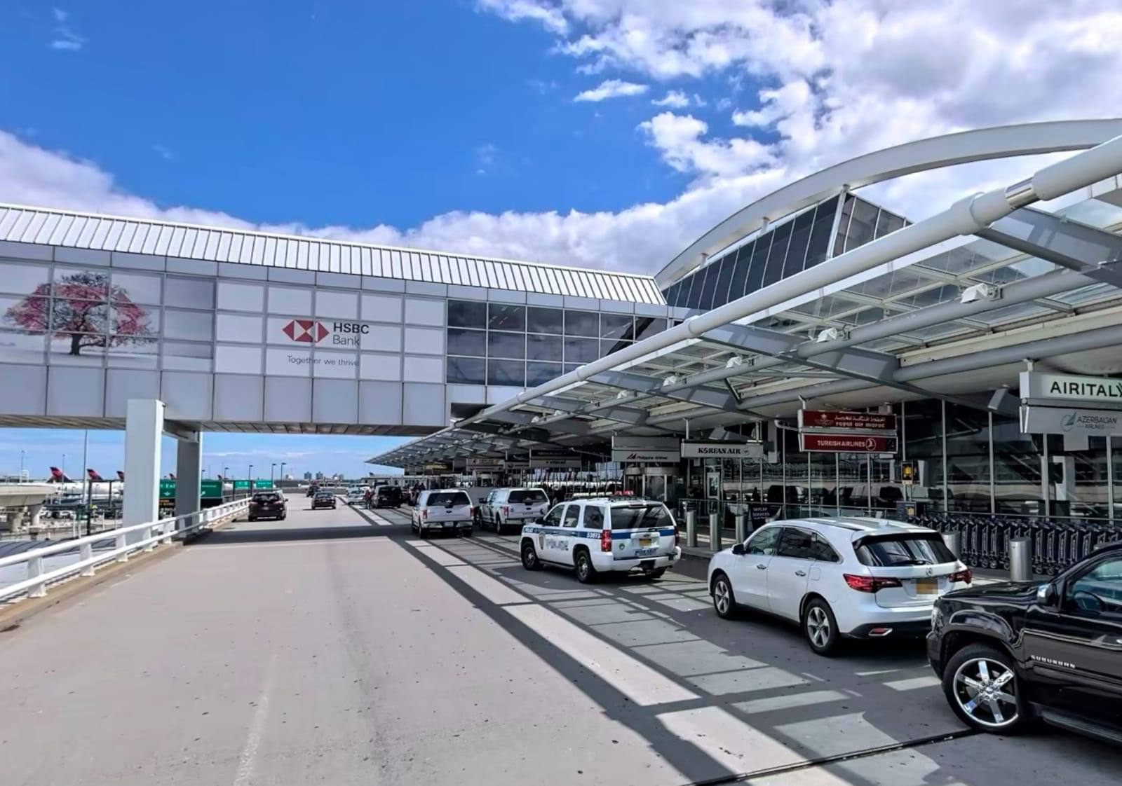 The JFK Terminal 1 departures curb, with airline check-in signs strung along the roadway under the arched glass canopy