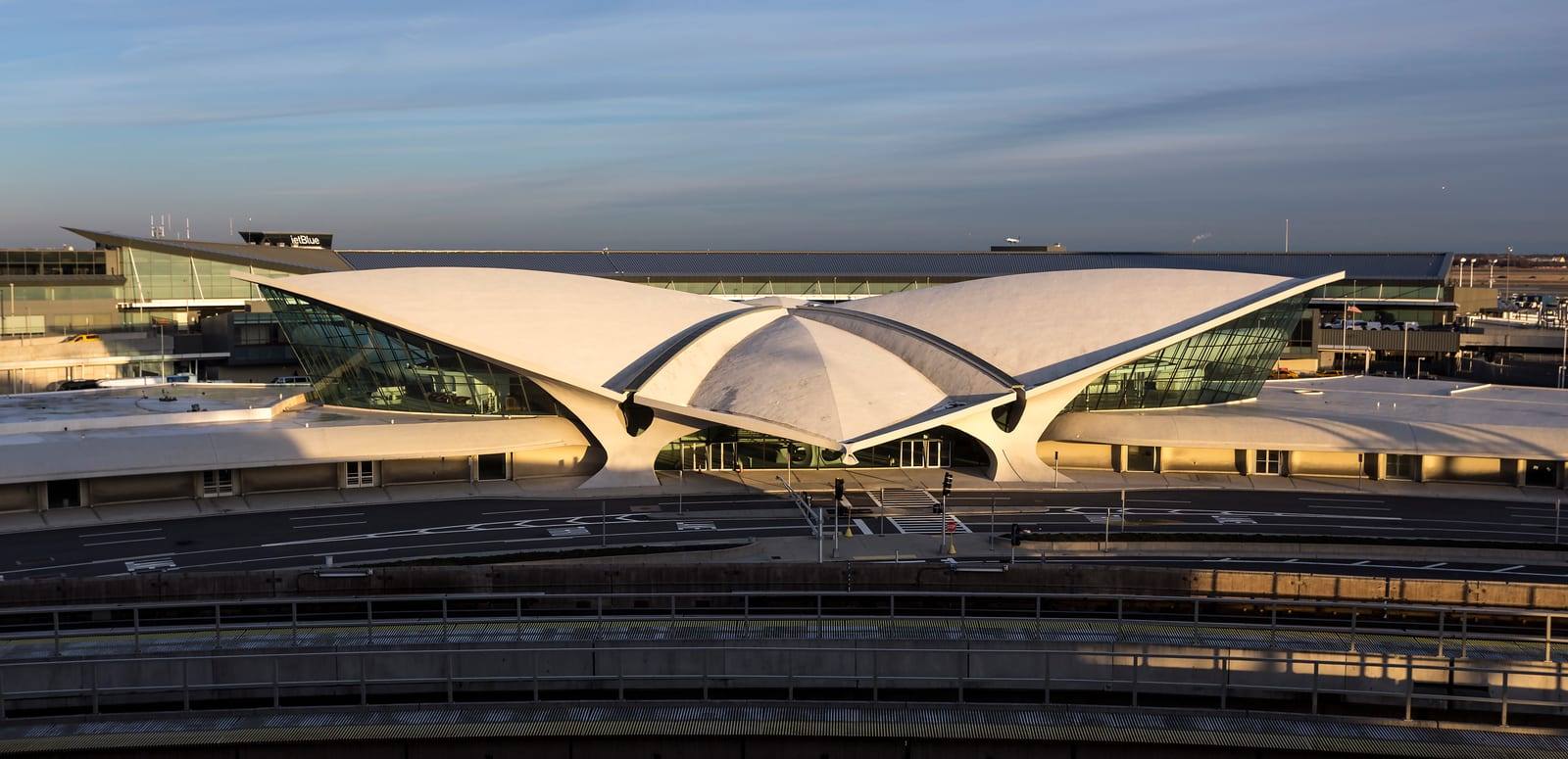 The TWA Flight Center at JFK airport, its winged concrete roof lit at sunset, with JetBlue’s Terminal 5 behind it